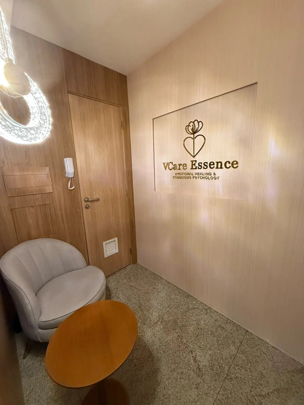 Entrada da VCare Essence, logo retroiluminado em parede de madeira e corredor com luz quente